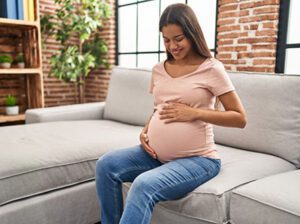 Pregnant Hispanic woman sitting on her couch thinking about her baby and adoption